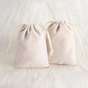 Close-up of two beige velvet drawstring pouches for jewelry storage on soft faux fur background