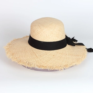 Detail of wide brim raffia sun hat featuring black ribbon bow and frayed tassel edges