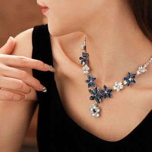 Detail shot of a silver necklace featuring blue and clear gemstone flower pendant on a model