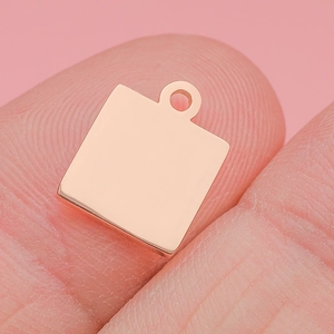 Macro view of a polished rose gold square pendant charm held on finger for scale