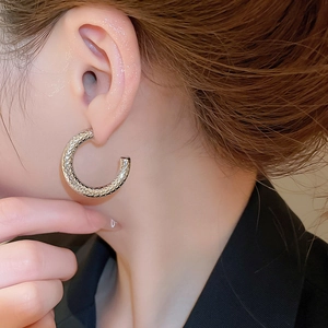 Close-up of a model wearing C-shaped silver textured metal earrings with a hammered finish