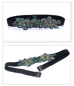 Detail of black elastic waist belt with green beaded flower and double metal snap buttons