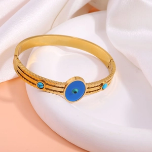 Detailed shot of golden evil eye bangle with turquoise stones on white ceramic tray