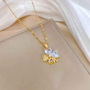 Macro detail of a gold clover necklace with heart-shaped zircon and pavé crystals