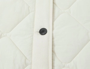Detail of diamond-quilted jacket with black button and herringbone placket texture