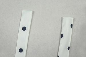 Detail view of the wide shoulder straps on a white sleeveless dress with large black polka dots