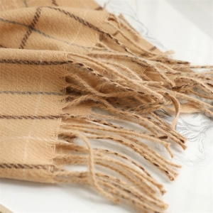 Detailed close-up of beige plaid scarf with soft cashmere texture and tassel fringe