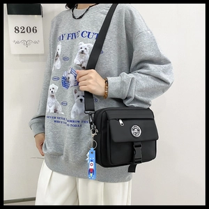 Detail of black nylon messenger bag featuring a buckle closure and blue rocket keychain
