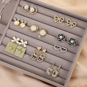 Small velvet jewelry tray displaying diverse pearl and floral earrings on grey fabric