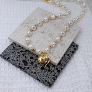 Detail of elegant pearl heart necklace featuring golden beads on a textured stone display