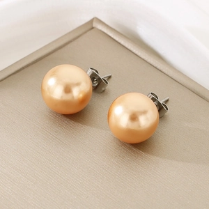 Close-up of champagne pearl stud earrings with polished metallic backs on a textured stand