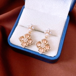 Detail of rose gold clover earrings with champagne zircon and white pearl on velvet