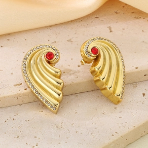 Macro detail of gold wing earrings with a central red stone and white crystal accents