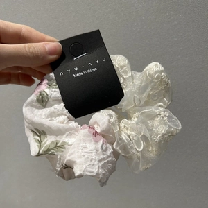 Detail of floral lace scrunchie with embroidery and ribbon on a branded card