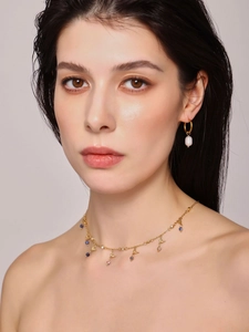 Close-up of gold necklace with blue charms and pearl drop earrings on a model