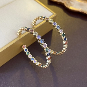 Close-up of golden C-shaped hoop earrings with rainbow colored cubic zirconia stones