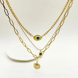 Macro detail of triple-layered gold stainless steel necklace with hamsa and coin pendants