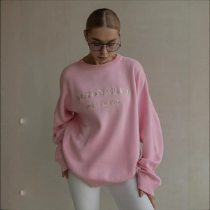 Detail of pink knitted sweater showing white ALSON CLUB embroidery and soft knit texture