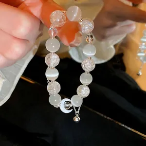 Cat eye stone bead bracelet with a crescent moon charm and silver bell on dark background