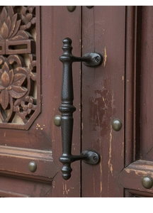 Detail of vintage black iron cabinet handle mounted on carved dark wood door