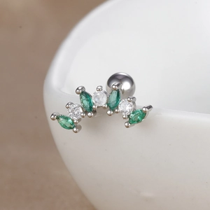 Gros plan d'un piercing d'oreille incurvé avec gemmes vertes et zircons transparents