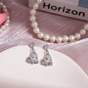 Détail de boucles d'oreilles cœur en argent avec cristal rectangulaire sur plateau blanc