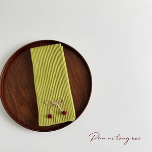 Detail of yellow-green knitted scarf with bow and cherry accents on wood tray