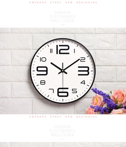 Modern black wall clock with bold digits hanging on a white brick wall with floral accent