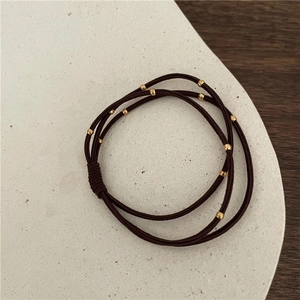 Detailed view of brown elastic hair tie with golden beads on a minimalist tray