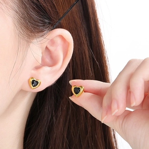 Gros plan de boucles d'oreilles cœur dorées avec pierre noire portées par un modèle