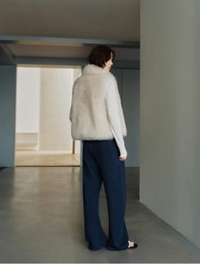 Detail of soft cream white faux fur vest texture on model in minimalist interior setting