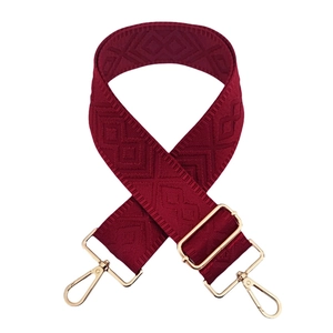 Detail of adjustable burgundy bag strap with woven geometric pattern and gold buckles
