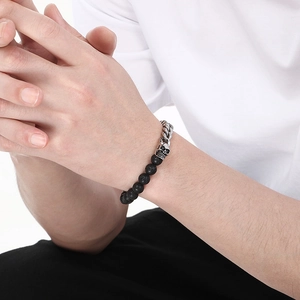Detail of men's skull bracelet with black lava stone and silver metal chain on wrist