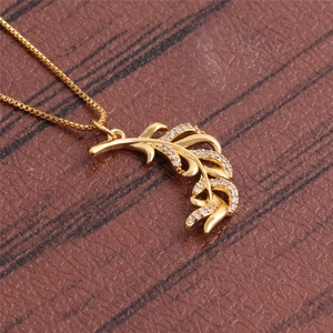 Macro shot of gold feather pendant with clear zircon on a brown leather surface