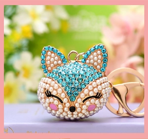 Macro shot of fox head keychain with blue rhinestones and white pearls on gold metal