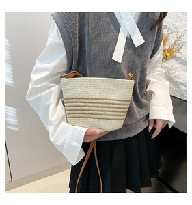 Detail of hand-woven straw crossbody bag with brown stripes on a model in minimalist setting