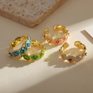 Golden open rings with colorful enamel flower patterns and diamonds on light background
