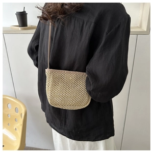 Dettaglio borsa a secchiello in paglia intrecciata beige indossata da una modella casual