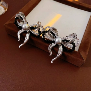 Detailed view of silver bow earrings with grey pearls and mixed black and white rhinestones