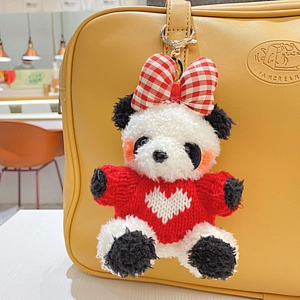 Porte-clés panda en peluche avec pull en tricot rouge sur un sac à main jaune vif