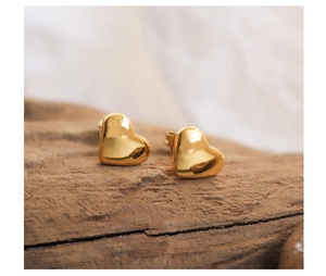 Detail of chunky gold heart stud earrings on a rustic wood background with polished finish