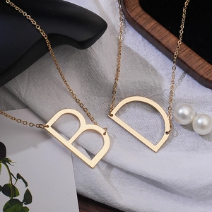 Close-up of elegant gold initial necklaces with letters B and D on a stylish white fabric