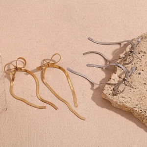 Close-up of gold and silver bow drop earrings with sleek metal snake chain tassels