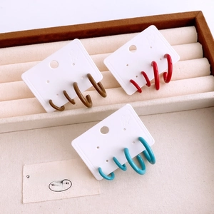 Close-up of geometric C-shaped earrings in red, brown and blue on a velvet tray