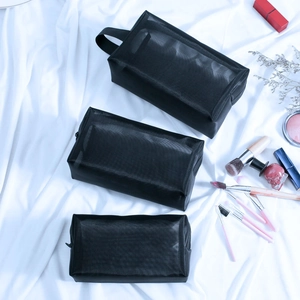 Three sizes of black nylon mesh makeup bags with cosmetics on white fabric background