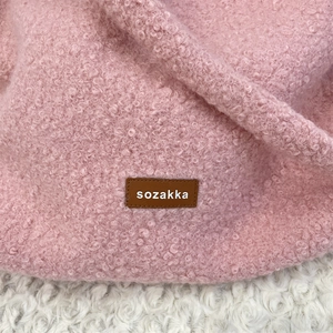 Close-up of pink faux shearling texture with a premium brown leather logo patch