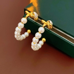 Detail of 18K gold plated pearl C-shaped earrings with a delicate bow knot design