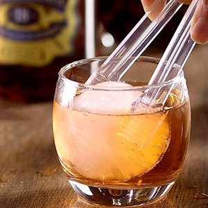 Pinza transparente recogiendo una bola de hielo redonda para un vaso de whisky