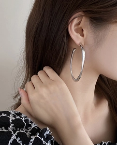 Close-up of a model wearing a large silver oval hoop earring in a minimalist metallic style