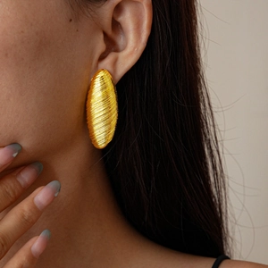 Detail view of gold textured oval earrings on model showing brushed metal surface